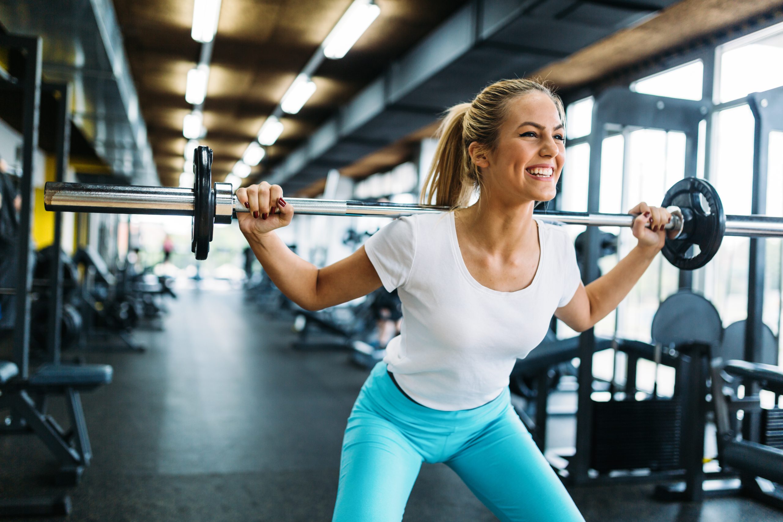 Beautiful active woman doing squats with weights in gym